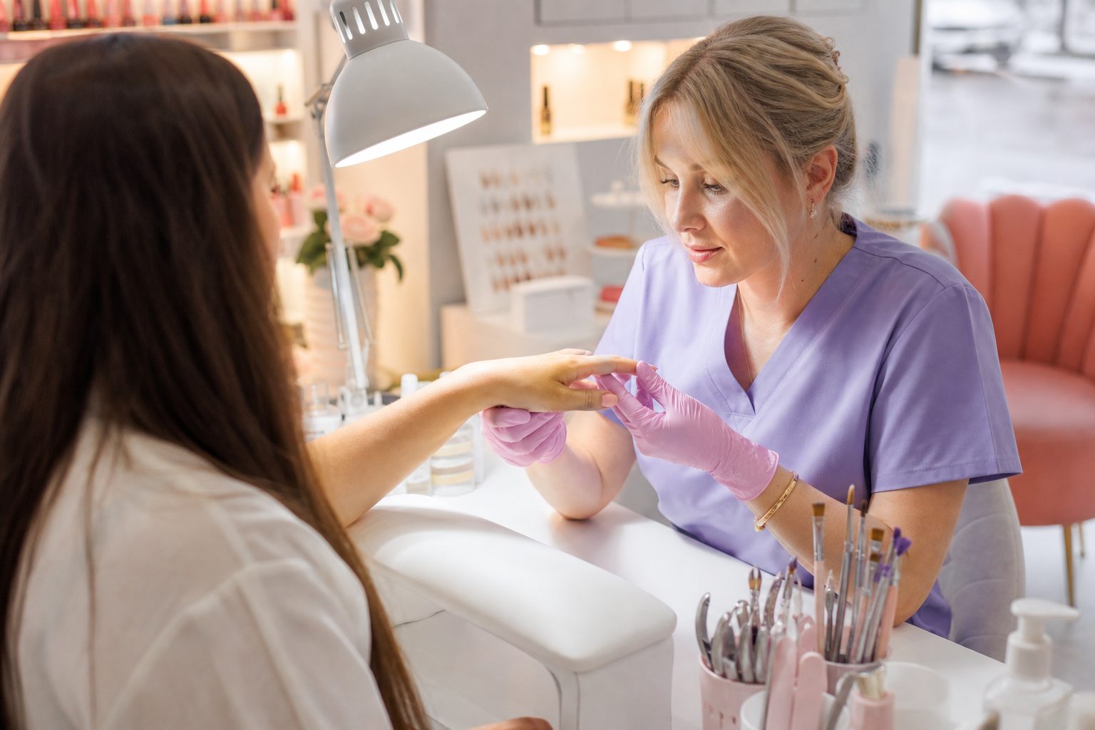 Nail technician inspecting a client's hand under a work lamp during a consultation