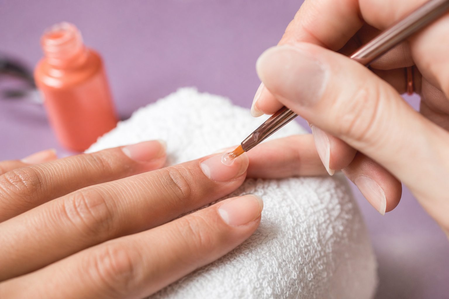 Close up of gel being applied thinly near the cuticle on a client's nail during a manicure